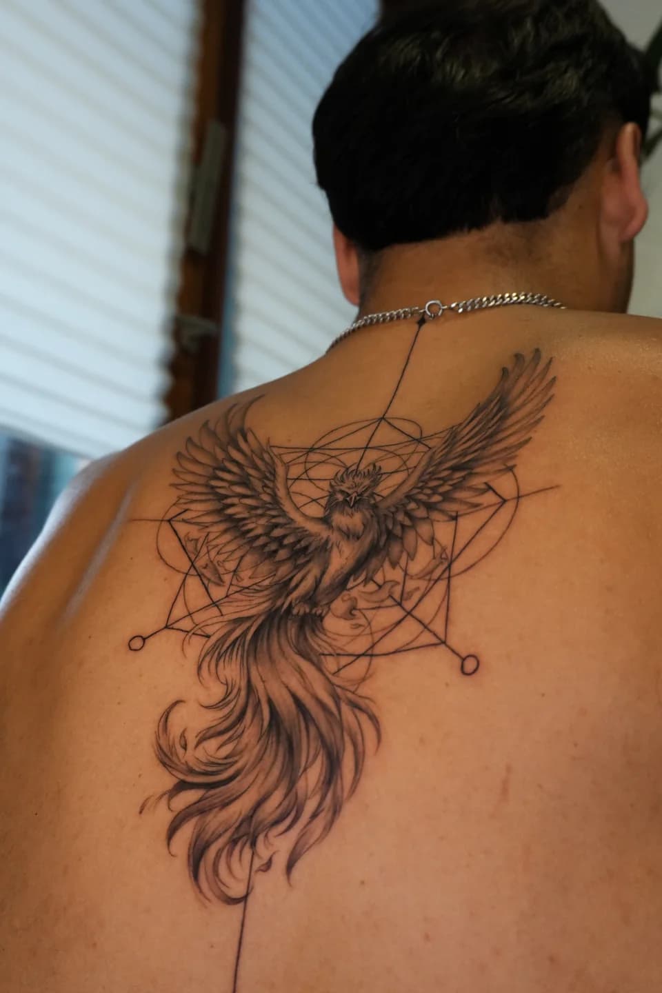 Fénix com elementos geométricos tatuada nas costas.