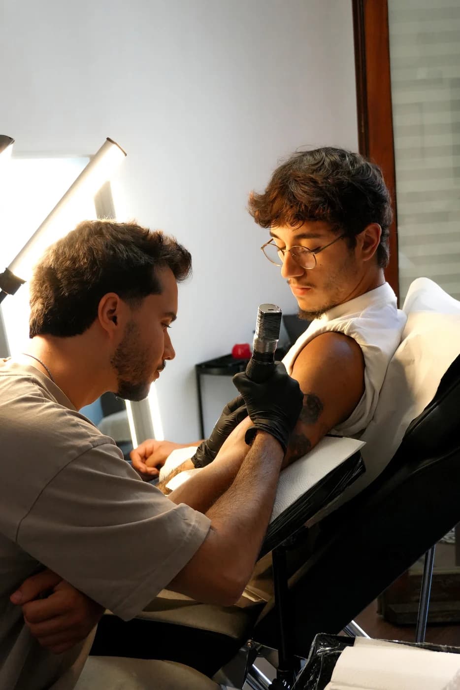 Daniel a tatuar o ombro de um cliente numa sala luminosa do estúdio.
